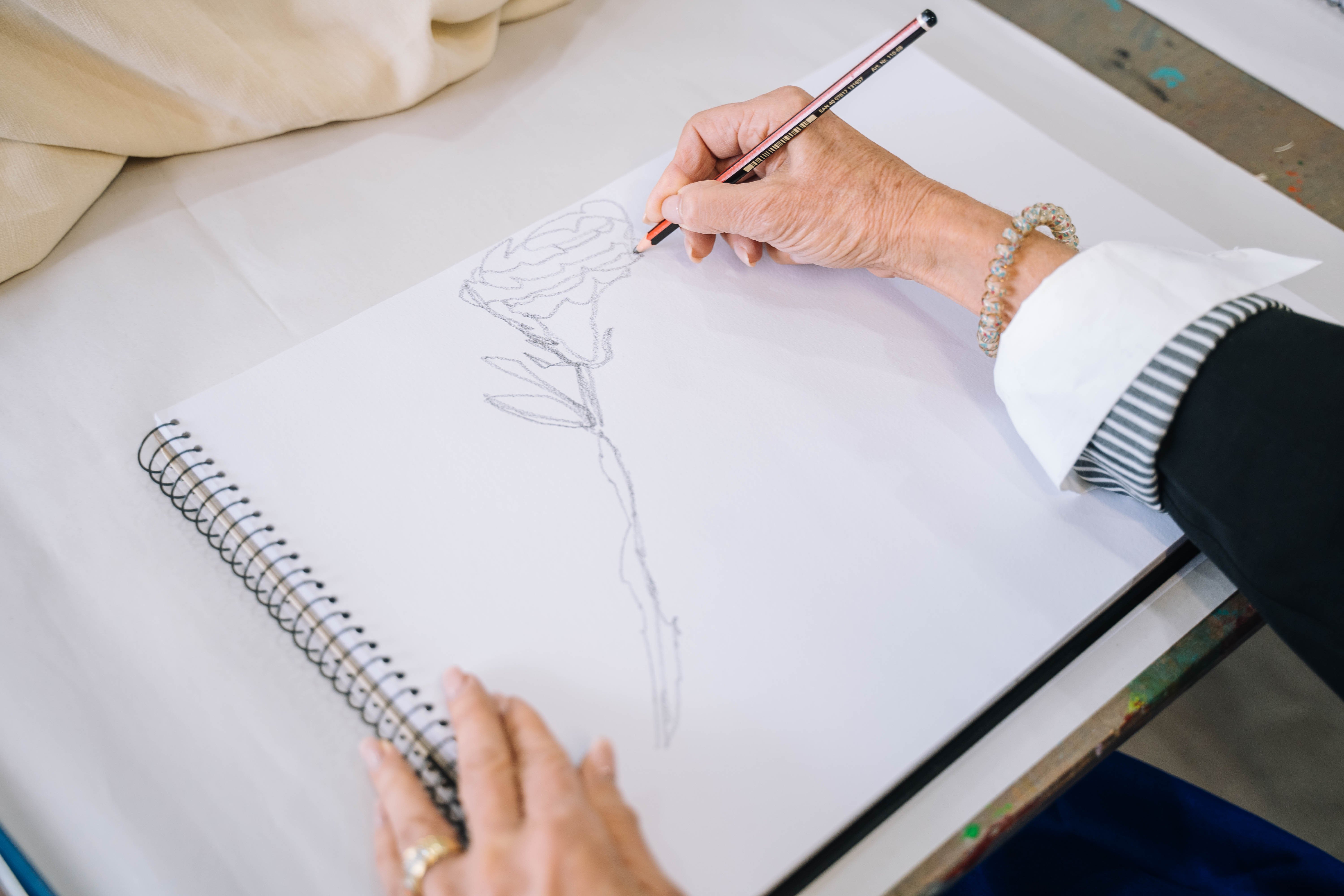 Person sketching a flower on a pad of paper